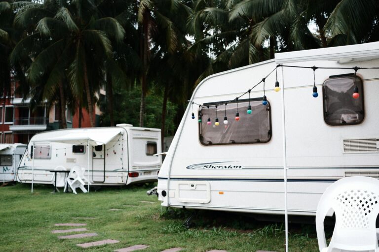 Relaxing caravan camping site under palm trees with outdoor seating and festive lights.